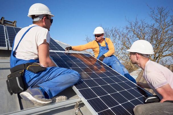 Tres electricistas montando módulo solar azul en el techo de la casa moderna
 - Foto, Imagen