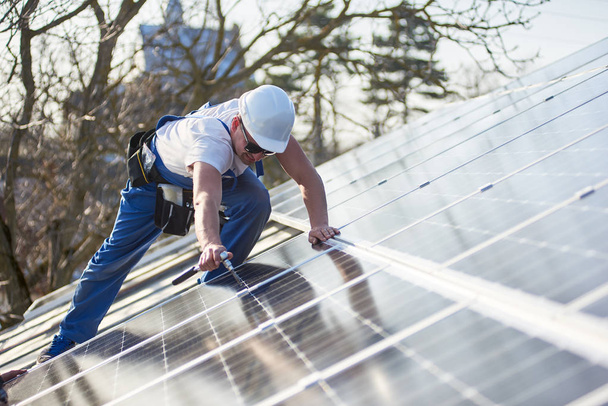 現代の家の屋根の上の青い太陽電池モジュールを取り付け電気技師。代替エネルギーの生態学的な概念. - 写真・画像