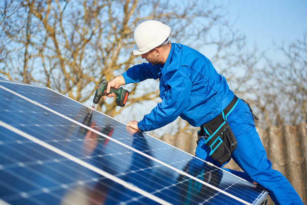 Ingenieur in blauem Anzug und Schutzhelm installiert Photovoltaikanlage mit Schraubenzieher - Foto, Bild