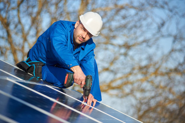 Ingegnere maschio in tuta blu e casco protettivo installazione impianto pannello fotovoltaico con cacciavite
 - Foto, immagini