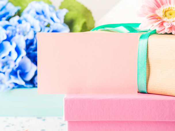 Tarjeta rosa en blanco y cajas de regalo apiladas. Flores
 - Foto, imagen