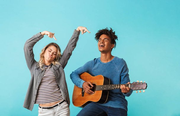 Happy young multiethninc couple together, playing a guitar isolated over blue background - Photo, image