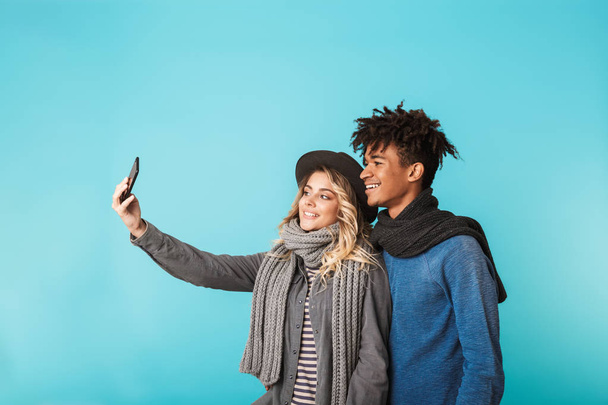 Happy teenage couple standing isolated over blue background, taking a selfie - Фото, изображение