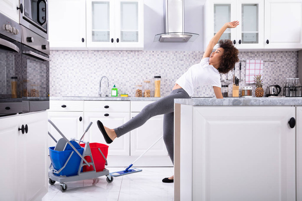 Lähikuva nuori afrikkalainen nainen liukastuminen kun Mopping lattia keittiössä
 - Valokuva, kuva