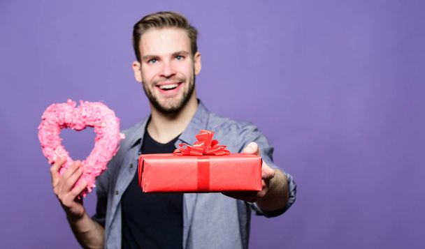 Valentines day gift. Romantic gift. Man with beard and happy face celebrate valentines day. Gift for girlfriend. Hipster hold gift box and heart violet background. Love and romantic feelings concept - Fotoğraf, Görsel