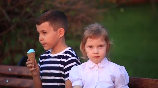 Μικρό αγόρι και το κορίτσι να κάθεται στον πάγκο και να τρώει ένα παγωτό - Πλάνα, βίντεο