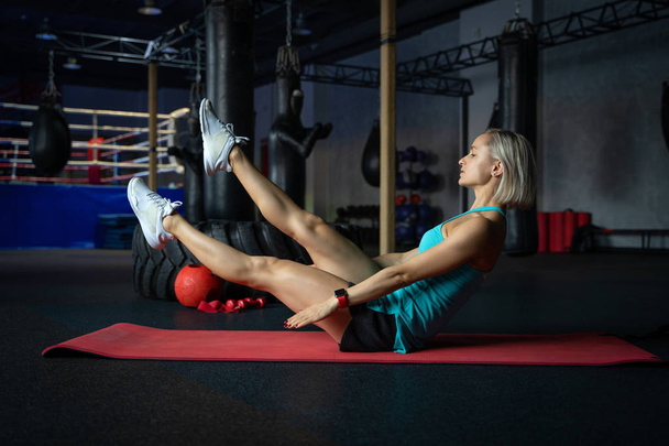 Young attractive cool woman practicing abs exercise, Sit Ups, working out, wearing sportswear, full length silhouette in boxing gym. - Foto, Imagem