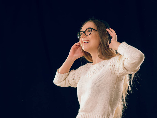 Piękna młoda kobieta korzystających słuchanie muzyki w bezprzewodowych słuchawek na ciemnym tle czarny - Zdjęcie, obraz
