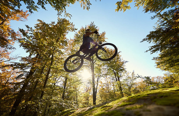 Low angle view of professional sportsman cyclist jumping on trial bicycle - Foto, imagen
