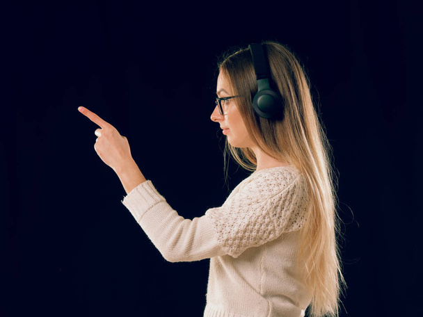 Mooie genieten van jonge vrouw luisteren van de muziek in draadloze hoofdtelefoon op donkere zwarte achtergrond - Foto, afbeelding
