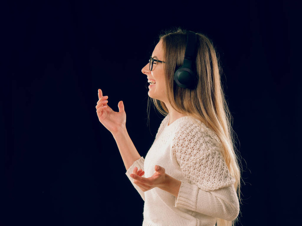 Молодая женщина слушает музыку в беспроводных наушниках на темном черном фоне
 - Фото, изображение