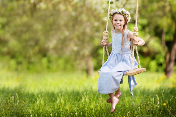 Schattig jong meisje op een schommel in de bloeiende oude apple tree tuin plezier. Zonnige dag. Lente outdoor-activiteiten voor kinderen - Foto, afbeelding