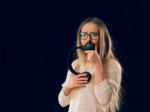 Молодая женщина слушает музыку в беспроводных наушниках на темном черном фоне
 - Фото, изображение