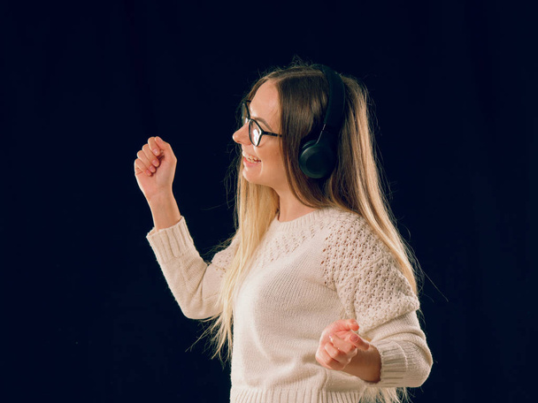 Linda desfrutando jovem mulher ouvindo a música em fone de ouvido sem fio no fundo preto escuro
 - Foto, Imagem