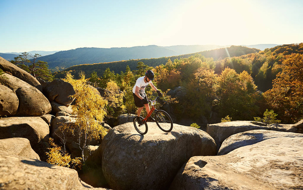 Joven ciclista masculino balanceándose en bicicleta de prueba sobre una gran roca
 - Foto, imagen