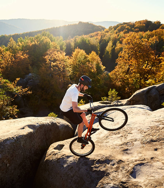Fiatal férfi kerékpáros tárgyalás kerékpár tetején nagy szikla kiegyensúlyozó - Fotó, kép