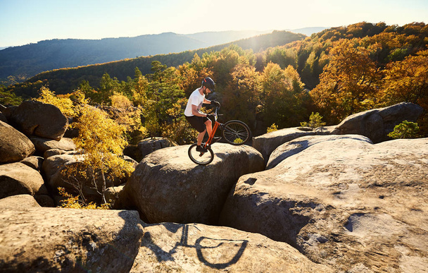 Jovem ciclista do sexo masculino balanceamento na bicicleta julgamento em cima de grande pedra
 - Foto, Imagem