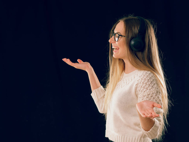 schöne junge Frau genießt die Musik in drahtlosem Kopfhörer auf dunkelschwarzem Hintergrund - Foto, Bild