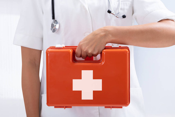 Mid-section Of A Doctor's Hand Holding Red First Aid Bag On White Background - Photo, Image