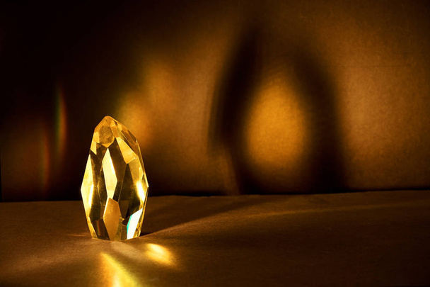 Raios de luz passando por um grande cristal de quartzo amarelo em um fundo marrom escuro
. - Foto, Imagem