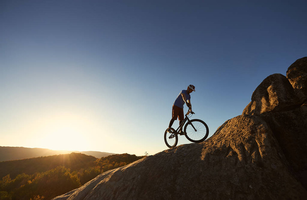 Silhueta de ciclista profissional balanceamento na bicicleta de teste em cima de pedregulho grande
 - Foto, Imagem