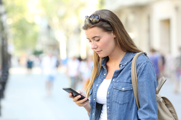 Single girl checking smart phone content standing in a city street - Foto, Imagem