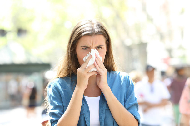 Front view of an ill or allergic woman blowing mucus looking at camera in the street - Foto, Bild