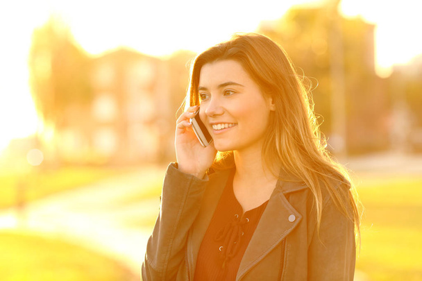 Happy teenage girl talking on phone at sunset in a park - Photo, Image