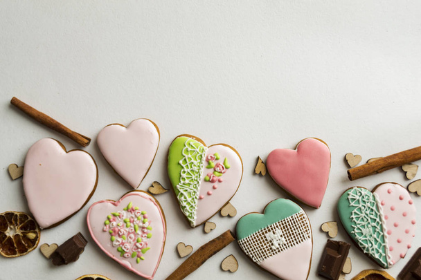 Painted gingerbread with cinnamon and hearts on a white background. gingerbread in pink glaze. Bakery products. Gingerbread in the shape of a heart. Place for text. Gingerbread pattern Background. - Photo, image