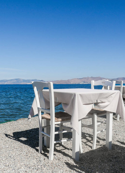 White restaurant tables on the beach in summer - travel, vacation and summer concept. The perfect lunch with a sea view - Fotografie, Obrázek
