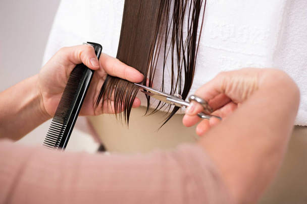 Cabeleireiro aparando o final de um cabelo de senhoras em uma visão de perto em suas mãos segurando um pente e a tesoura
 - Foto, Imagem