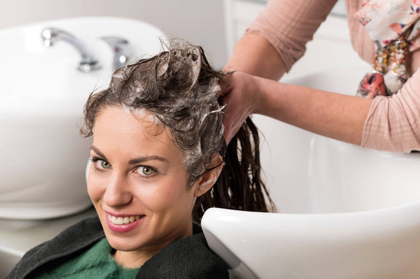 Atraktivní žena s vlasy umýt v umyvadle v profesionální kadeřnictví v zblízka pohled na její tvář a ruce šamponování vlasy - Fotografie, Obrázek
