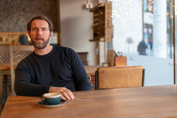 Middle aged caucasian male sitting at the table in coffee shop expressing disbelief and dislike - Foto, Bild