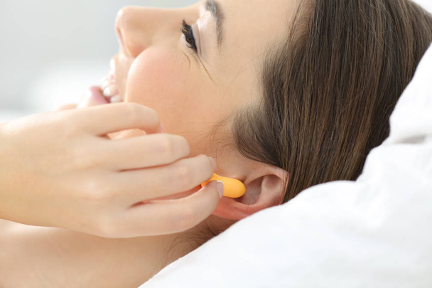 Close up of a woman hand putting ear plugs to sleep on a bed at home - Foto, Imagen