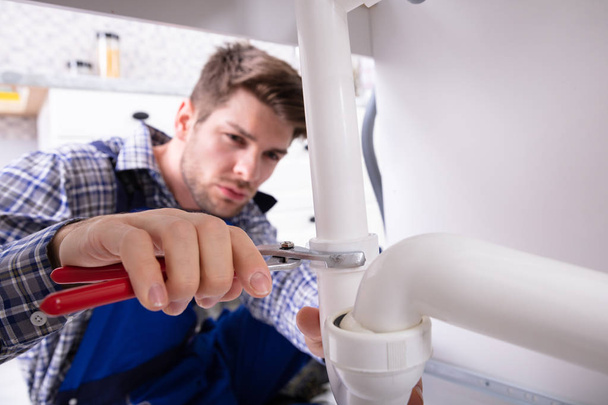 Young Male Plumber Repairing Sink Pipe With Adjustable Wrench - Foto, afbeelding