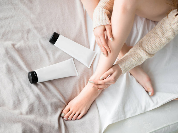 Vrouwelijke voeten en huid verzorging crème in buizen op het bed. Huid zorg concept - Foto, afbeelding