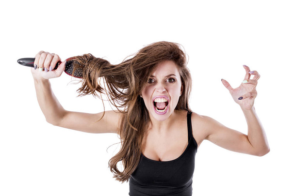 schattig meisje trekt een kam van verwarde haren en geschreeuw in de camera op een witte achtergrond. Haar gezondheid concept. - Foto, afbeelding