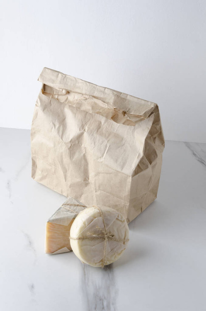 Κατακόρυφη βολή. Οικολογική τσάντα με φρέσκα και νόστιμα διαφορετικά είδη τυριού στο λευκό μαρμάρινο τραπέζι - Φωτογραφία, εικόνα