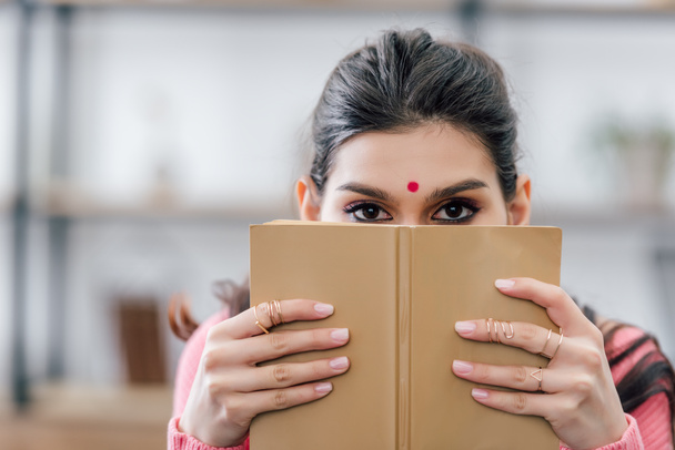 ινδική μαθητής με bindi κρατώντας βιβλίο μπροστά από το πρόσωπο - Φωτογραφία, εικόνα