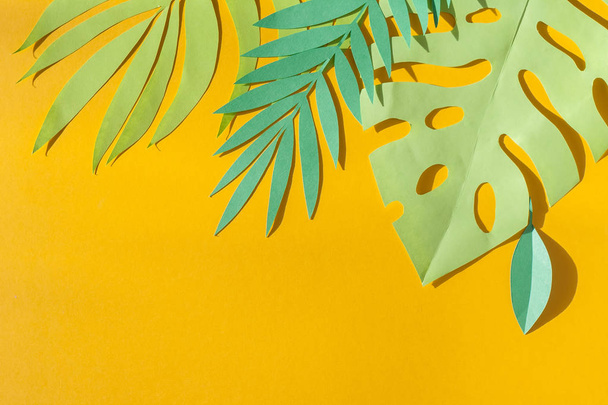 Green tropical leaves cut from paper in the sun rays on a yellow background. Summer concept - Foto, afbeelding