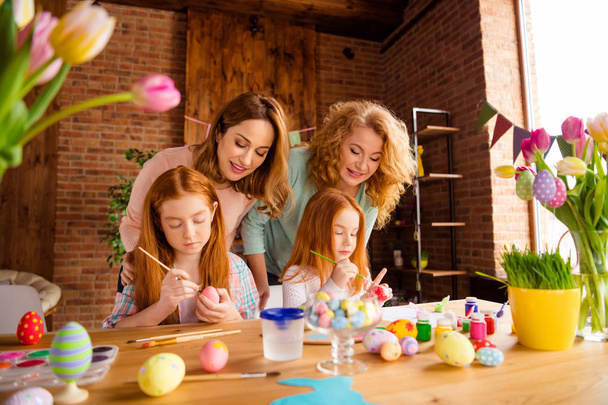 Portrait of two nice attractive cheerful ladies helping assisting two girls doing decorative things dying eggs in house brick loft industrial interior room indoors - Foto, Bild