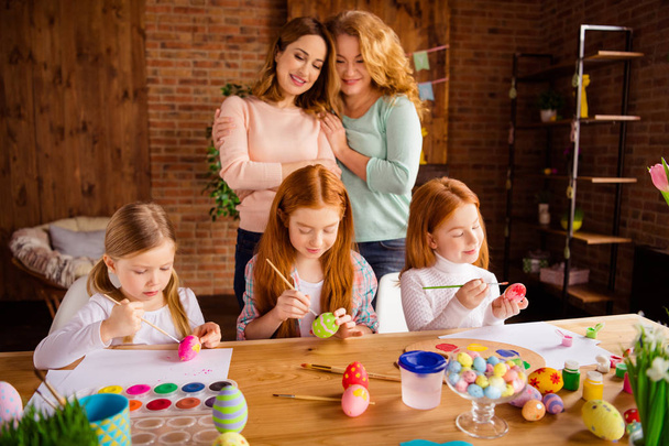 Portrait of nice attractive cheerful ladies helping assisting girls doing making decorative things dying eggs youth in house brick loft industrial interior room indoors - Foto, imagen