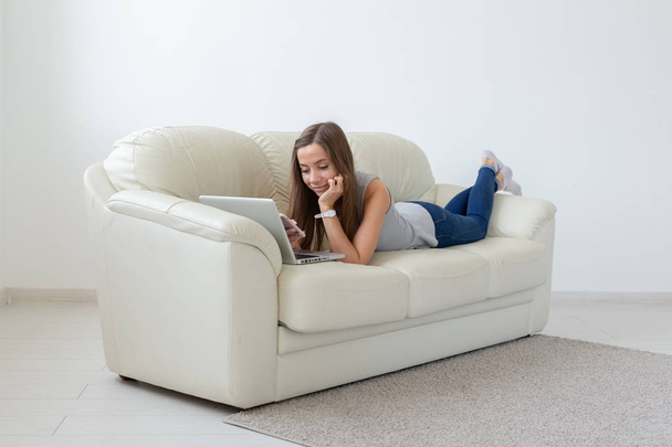 Technologie, zrelaksować się i zewnętrznych, koncepcja - młoda kobieta, leżąc na kanapie i pracę na laptopie - Zdjęcie, obraz