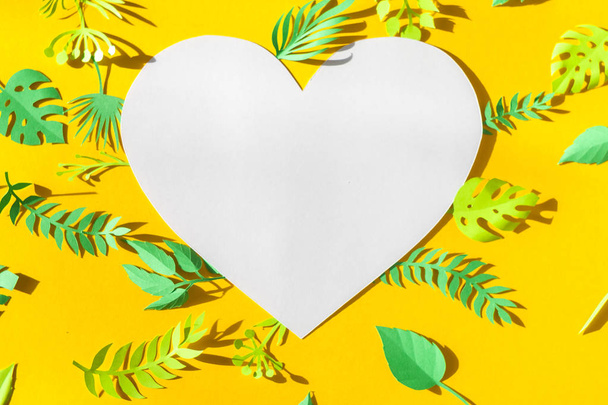 Heart frame with reen tropical leaves cut from paper in the sun rays on a yellow background. Summer concept - Foto, Imagen