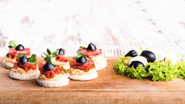 Herkullisia kanapeja salamin, oliivien ja mausteiden kanssa puupohjalla
 - Valokuva, kuva