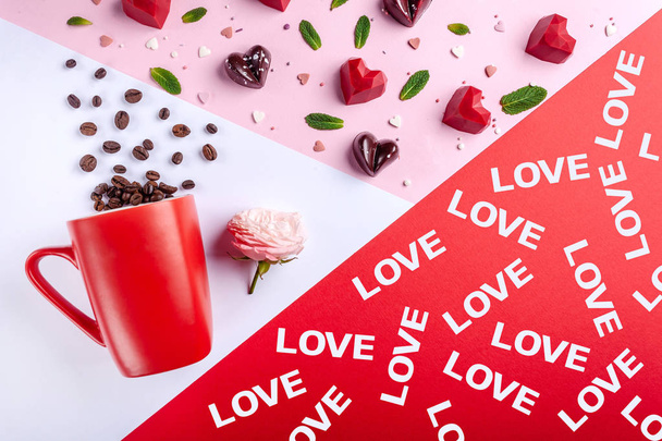 Bögre, szemes kávé, pink rose és csokoládé cukorka szív alakú, felső kilátás. Valentin-nap romantikus üdvözlőlap, kreatív lapos feküdt édesség élelmiszer és mentalevél összetétele - Fotó, kép