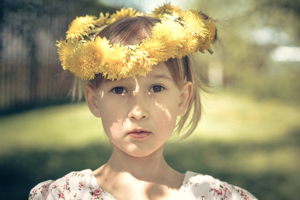 little cute caucasian girl with dandelion wreath in garden - Foto, Imagen