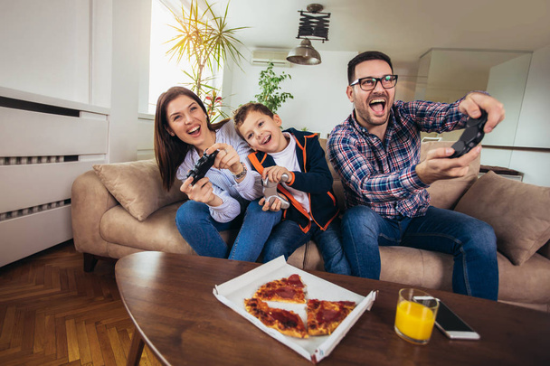 glückliche Familie sitzt auf einem Sofa und spielt Videospiele und isst Pizza - Foto, Bild