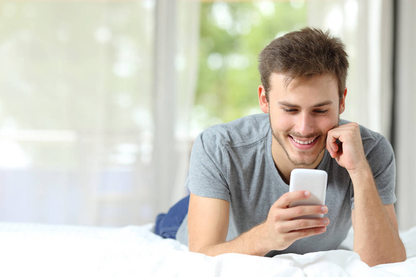 Vooraanzicht van een gelukkig man met behulp van slimme telefoon op het bed met kopie ruimte - Foto, afbeelding