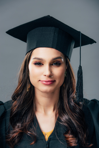 smiling indian student in academic gown and graduation cap, isolated on grey - Photo, Image